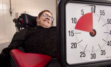 Titia de Haan zit in rolstoel en kijkt lachend naar de klok met timer