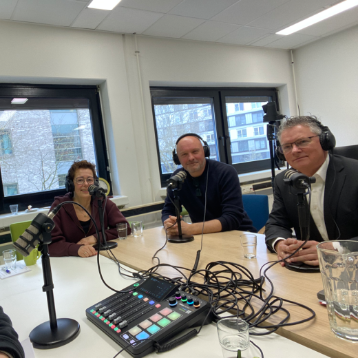 vier mensen zitten aan en tafel met koptelefoons op achter een microfoon