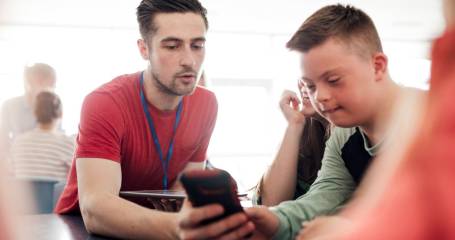 Medewerker begeleidt jongen met het syndroom van Down op de mobiel