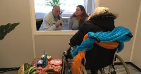 mevrouw in rolstoel praat met man en vrouw via raam bij Bartimeus