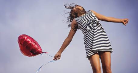 meisje met rode ballon in gestreepte jurk sprint in de lucht