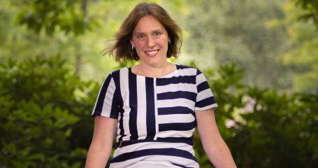 Karin Seijdell zit buiten en kijkt lachend in de camera