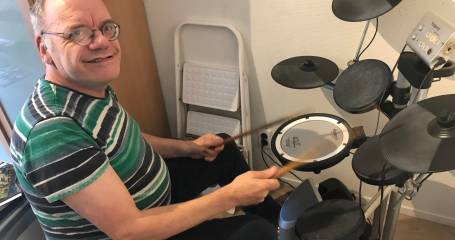Man zit achter elektrisch drumstel en kijkt lachend naar camera
