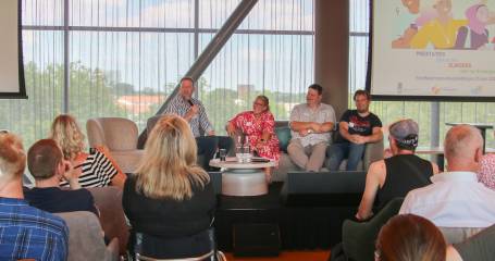 zaal vol mensen van de achterkant gefografeerd, kijkend naar een podium