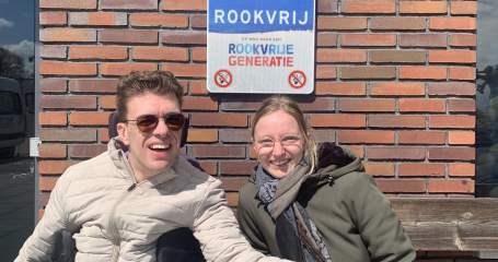 man in rolstoel naast hurkende vrouw onder een Rookvrij-bord