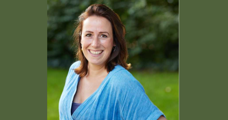 vrouw kijkt lachend in de camera voor een bosrijke omgeving