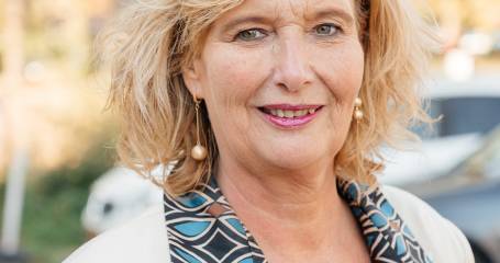 Blonde vrouw staat buiten en kijkt lachend in de camera