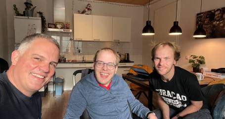 drie lachende mannen in een huiskamer kijken in de camera