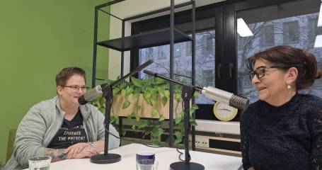 Maria en lindsey zitten achter een microfoon en lachen naar elkaar