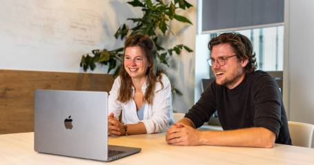 Twee personen achter een laptop die een webinar volgen