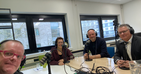 vier mensen zitten aan en tafel met koptelefoons op achter een microfoon