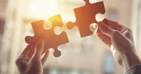 handen houden twee puzzelstukjes in het zonlicht