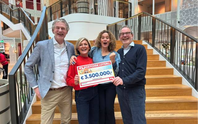 Vier mensen kijken lachend in de camera en houden een checque vast van 35000000 euro van de postcodeloterij