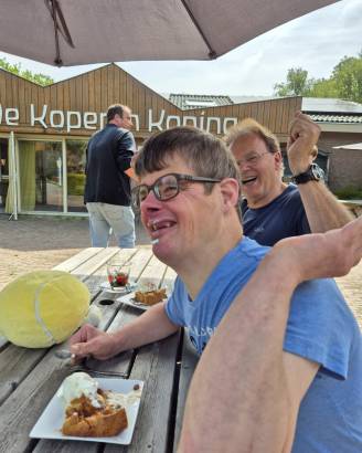 Henk en Jouke zitten lachend en etend aan een picknicktafel