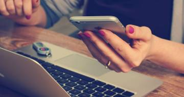 Vrouw achter laptop met iphone in haar hand