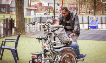Jongen in rolstoel wordt geholpen door een begeleider