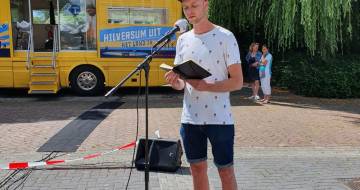 Levi Noe staat achter een microfoon in de buitenlucht om zijn gedicht voor te lezen