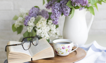 boek ligt open met bril erop op tafel met vaas paarse bloemen