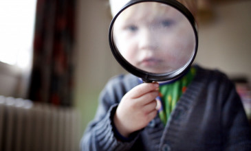 kind kijkt door vergrootglas naar camera