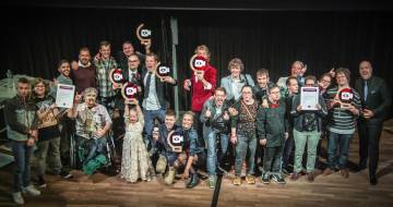 grote groep mensen staat op een podium en kijken in camera