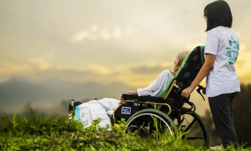 vrouw duwt rolstoel richting zonsondergang