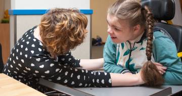 Jonge vrouw in rolstoel kijkt lachend naar vrouw die haar hand vastpakt