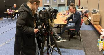 cameravrouw en mensen achter een bureau in gymzaal