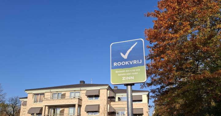 Een gebouw en grasveld en in het gras staat een bord met de tekst 'rookvrij'
