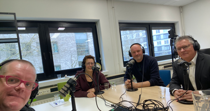 vier mensen zitten aan en tafel met koptelefoons op achter een microfoon