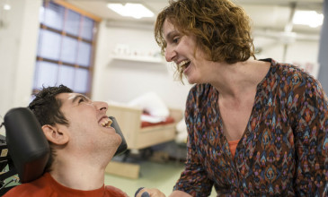 vrouw lacht naar jongen met beperking in rolstoel