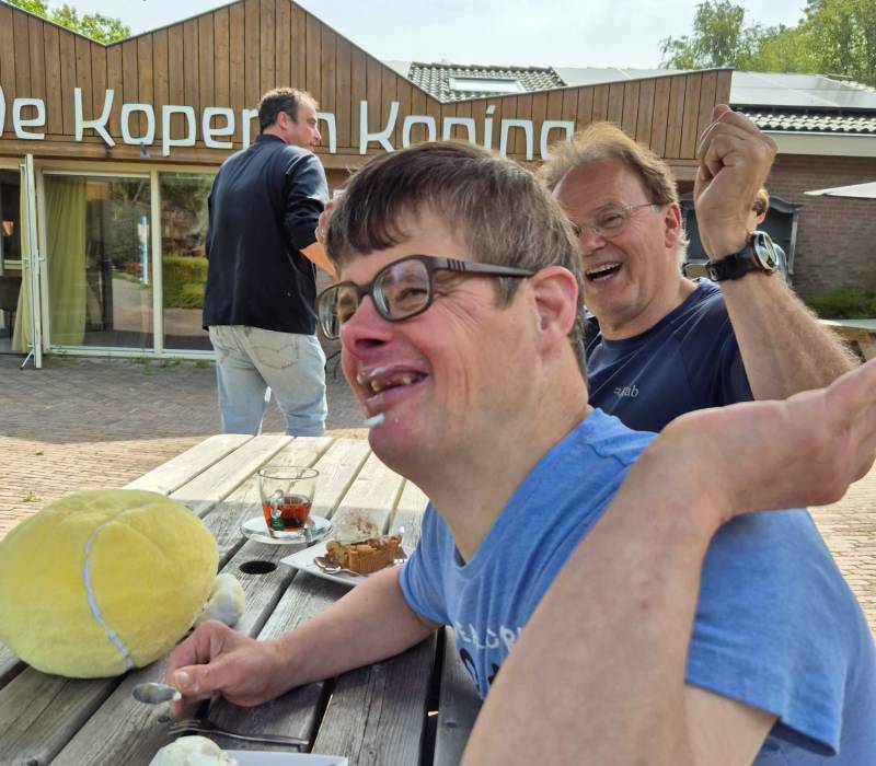 Henk en Jouke zitten lachend en etend aan een picknicktafel