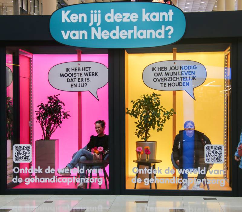 Een roze en oranje etalage met de tekst Ken jij deze kant van Nederland erop en in de etalege zitten twee vrouwen
