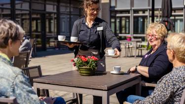 Vrouw serveert koffie uit aan gasten aan tafel