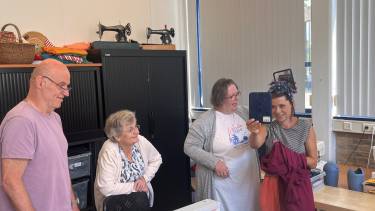 Lisa westerveld met haarband vol bloemen kijkt lachend in een spiegel terwijl twee dames en een heer lachend toekijken