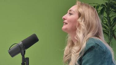 Ellen van Vliet zit achter een microfoon en lacht