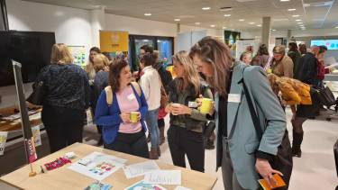 Mensen staan rond tafels met flyers erop te kijken en te prateen