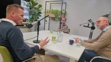 Jan Peter, Mike en Johan zitten aan tafel achter microfoons en zijn met elkaar in gesprek