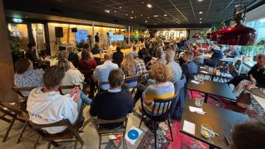 Zaal met deelnemers bijeenkomst generatieve AI en menswaardige zorg tijdens de presentatie van een praktijkvoorbeeld