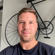 Tjerk Jonkers kijkt lachend in de camera in zijn huis. op de achtergrond is een fiets te zien.